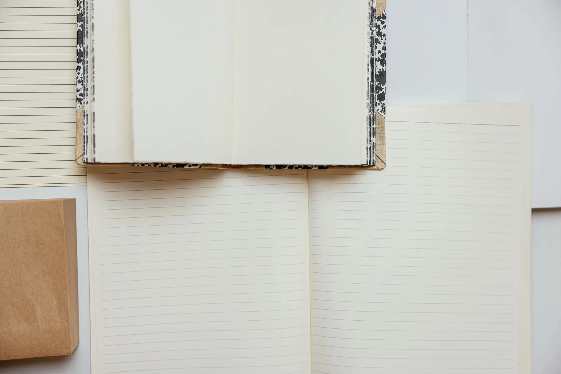 Trois carnets ouverts aux pages lignées blanches, avec couvertures en carton kraft et motifs géométriques noirs et blancs