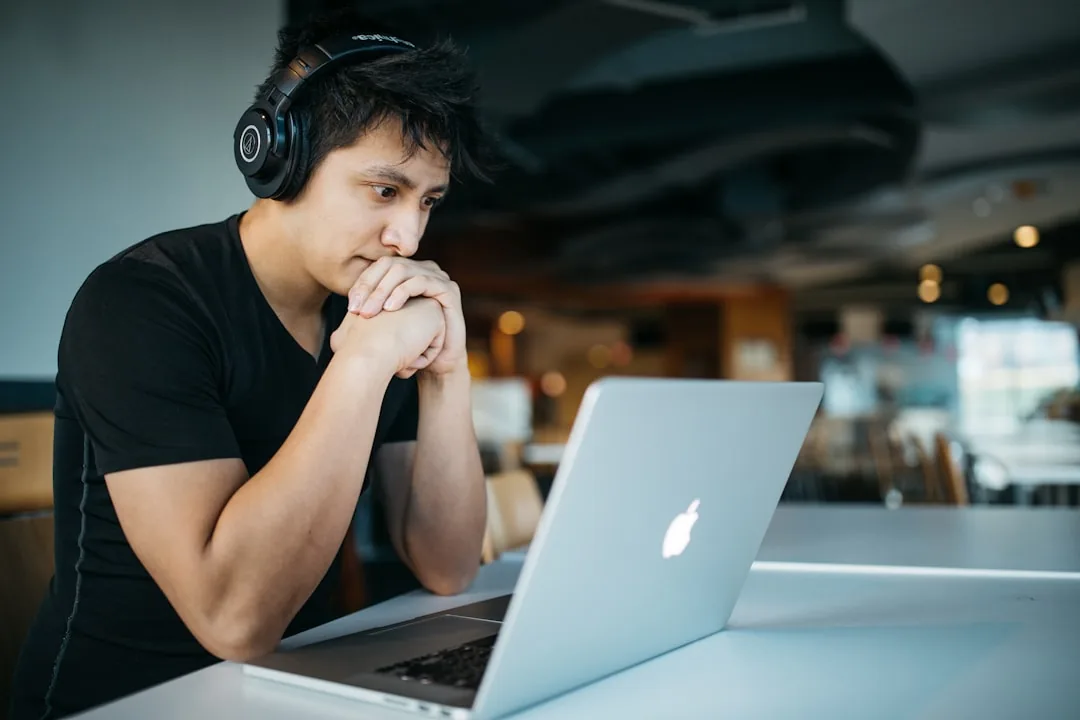 Personne avec casque audio devant un ordinateur portable, main au visage, en posture concentrée