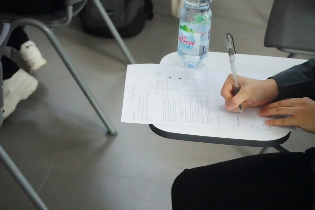 Une personne écrit sur une feuille de test posée sur un petit bureau de chaise