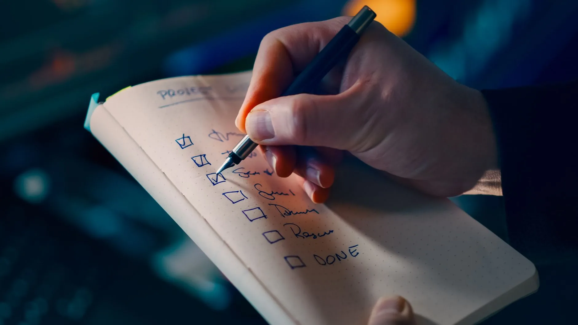 Main écrivant une liste de tâches à cocher dans un carnet ouvert, stylo en main